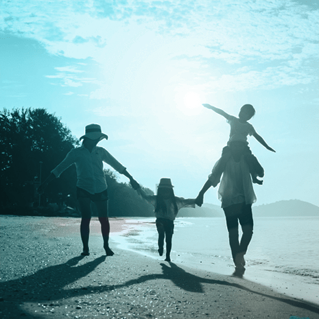 Family of four walking along a beach holding hands.