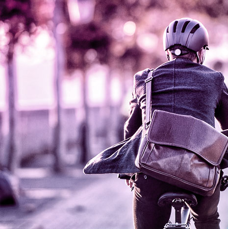 Man from behind riding a bicycle with a satchel on his back.