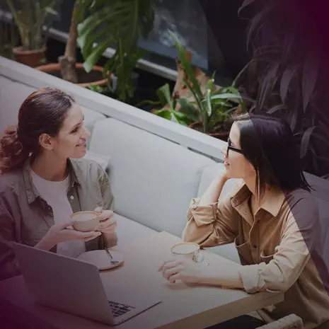 Two women talking and drinking coffee with laptop on the table.