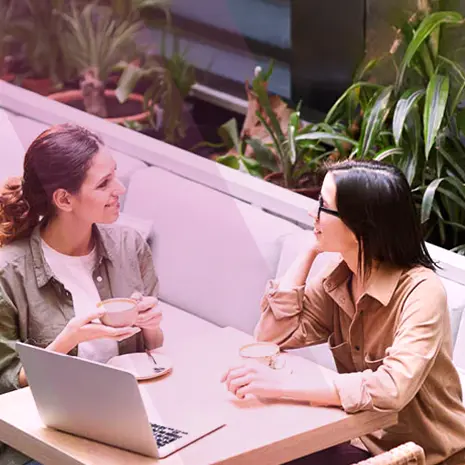 Two women talking and drinking coffee with laptop on the table.